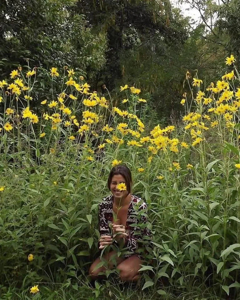 Kara Escande smiling among yellow flowers, holding a flower